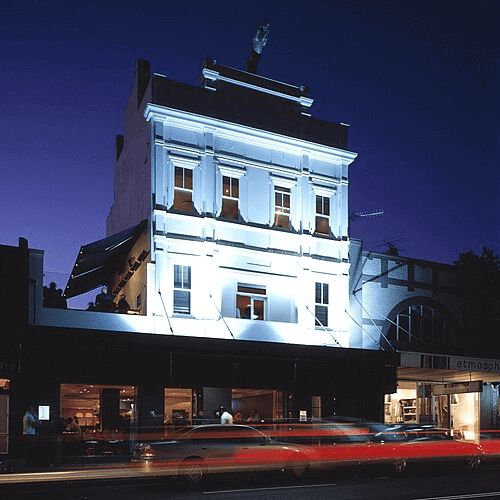 A white building in Surry Hills, Sydney with a red car driving past