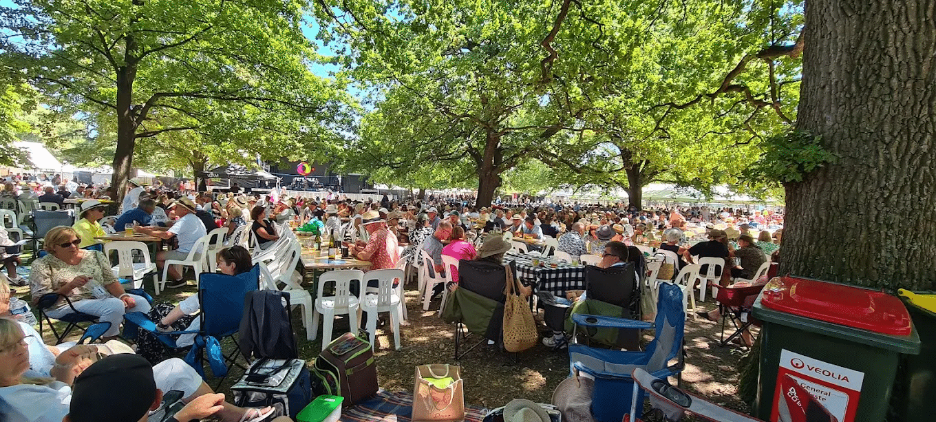 A large gathering seated outdoors under trees
