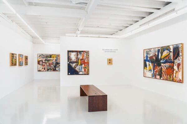 A white room showcasing paintings and a wooden bench at a Brisbane art attraction