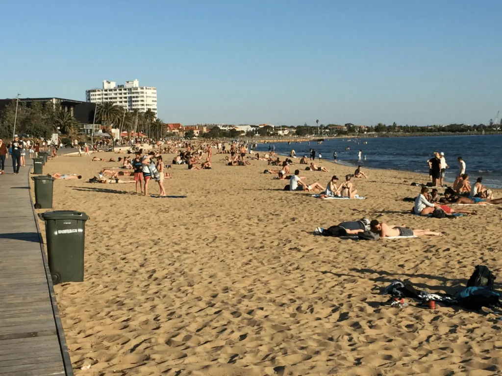 Crowded beach scene in Melbourne with people lounging on sand