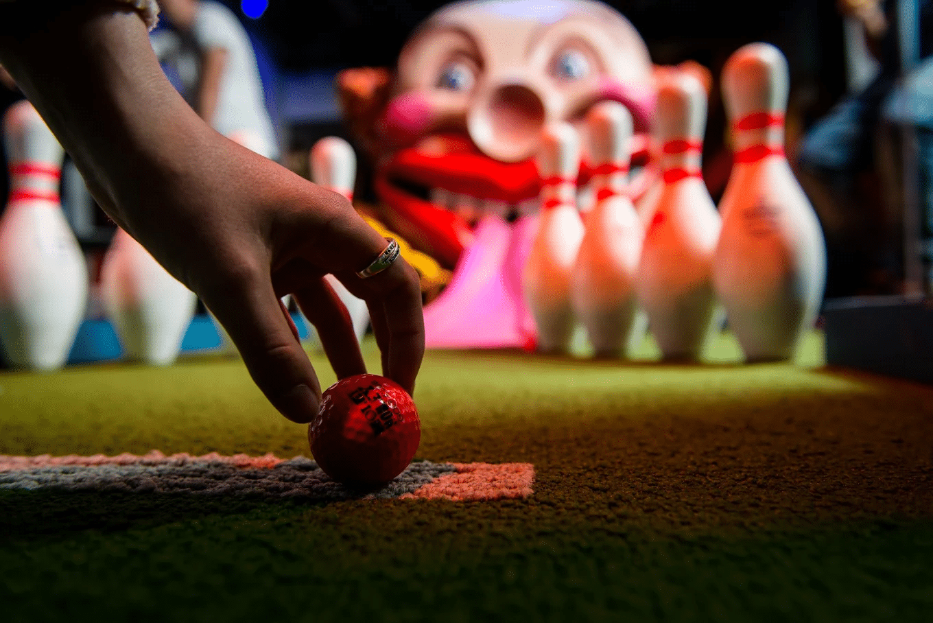 Hand reaching for red bowling ball with pins in background