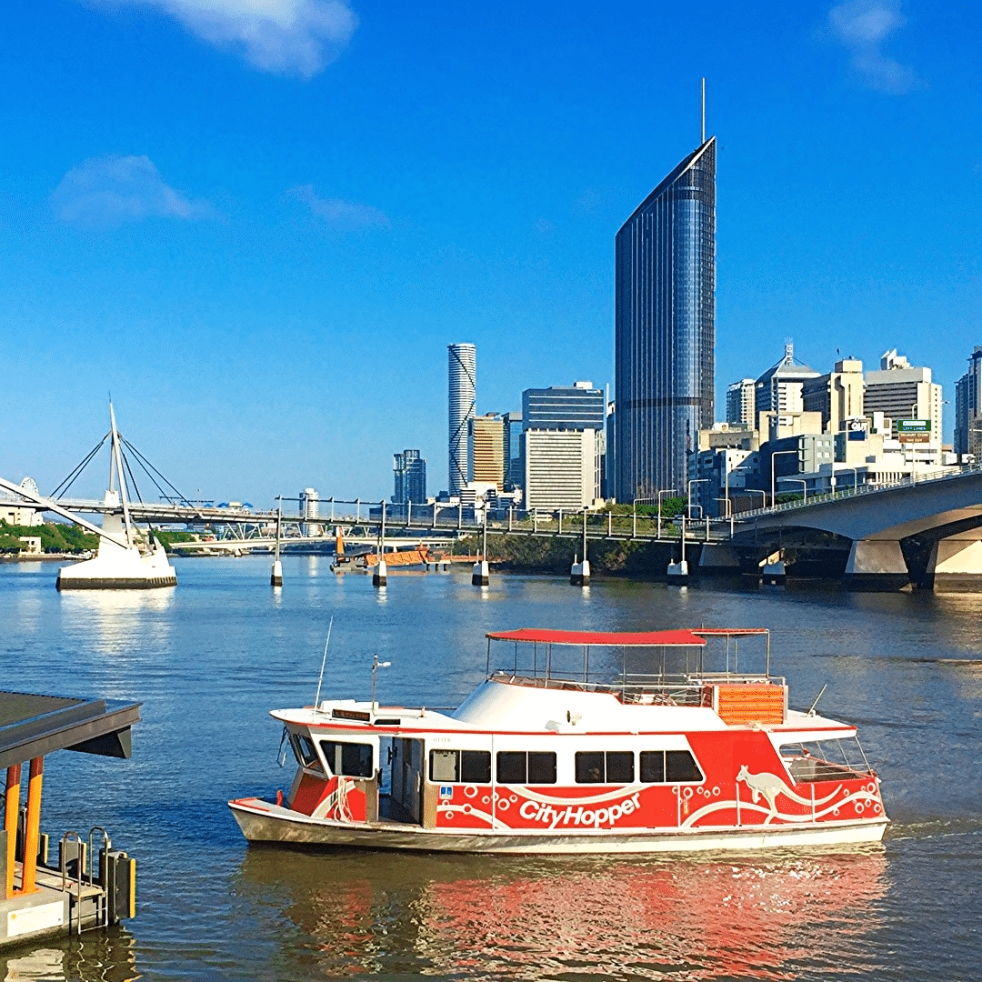 Red and white boat on river near Brisbane cityscape