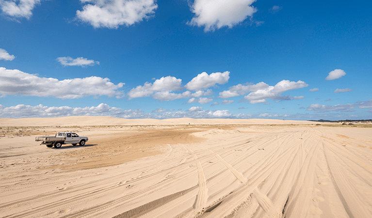 Truck driving in sandy area under blue sky